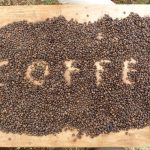 Das Bild zeigt eine Menge geröstete Kaffeebohnen auf einem Holztisch. In die Kaffeebohnen hat ein Witzbold mit den Fingern "Coffee" reingeschrieben.