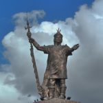 Das Bild zeigt die Statue des alten Inka-Fürsten Pachacútec . Sie ist aus Bronze gefertigt. Der Mann steht in geöffneter Pose zur Kamera hin, hat den linken Arm mit offener Handfläche etwas seitlich ausgestreckt. Die linke Hand hält einen geschmückten Speer, welcher den Fürsten etwas überragt. Hinter der Statue ist Himmel zu sehen, der von Wolken geprägt ist. Lediglich im Teil links und mittig oben ist ein wenig blauer Himmel zu sehen.