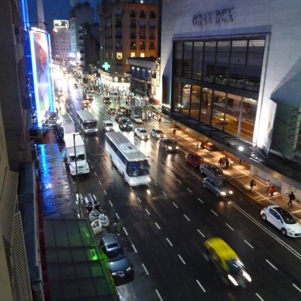 Das Bild zeigt eine Straße einer Großstadt bei Nacht. Es sind Hochhäuser zu erkennen, Autos und Busse, die mit Lichtern auf der Straße fahren.