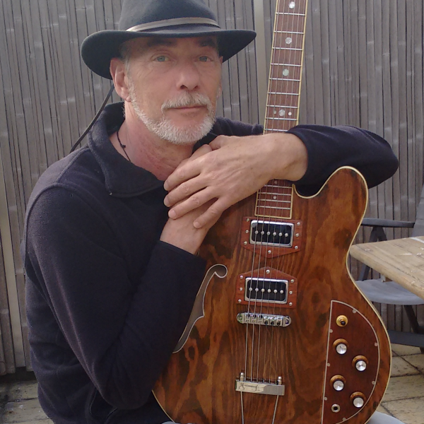 Das Bild zeigt einen Mann mit einem Hut auf dem Kopf und einer elektrischen Gitarre in den Händen.